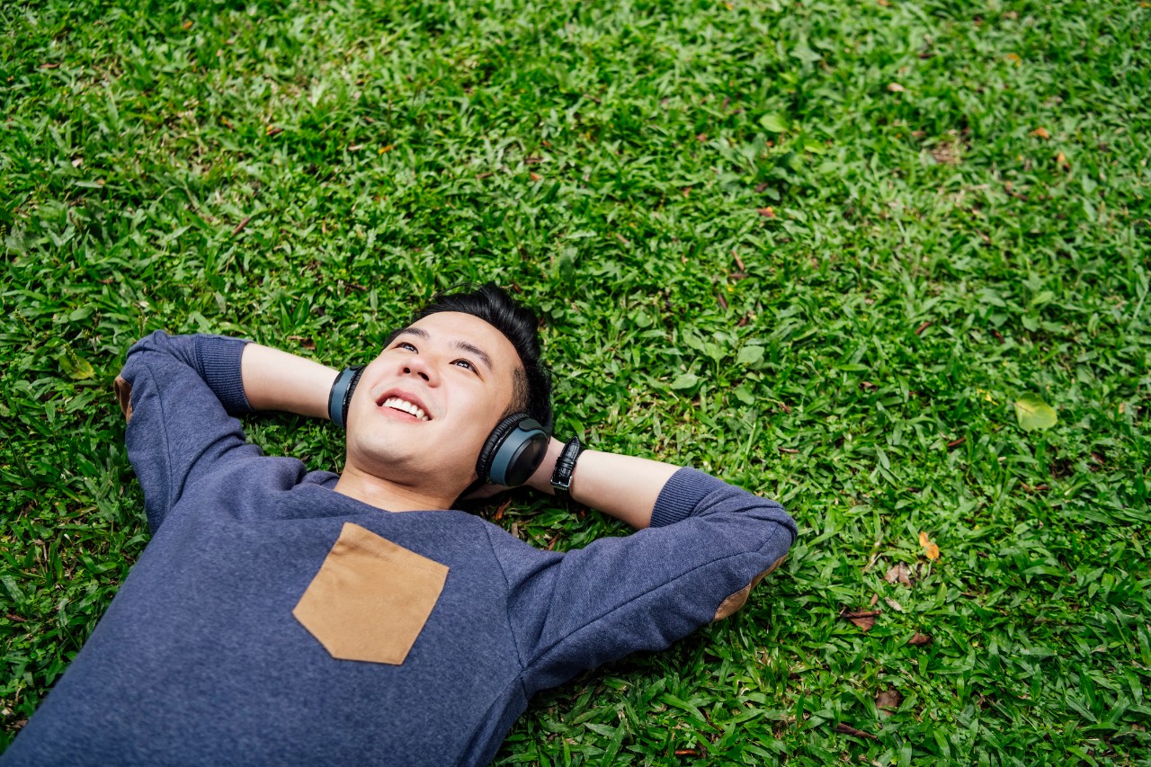 Man lays relaxed on the grass and undistracted from achieving financial goals